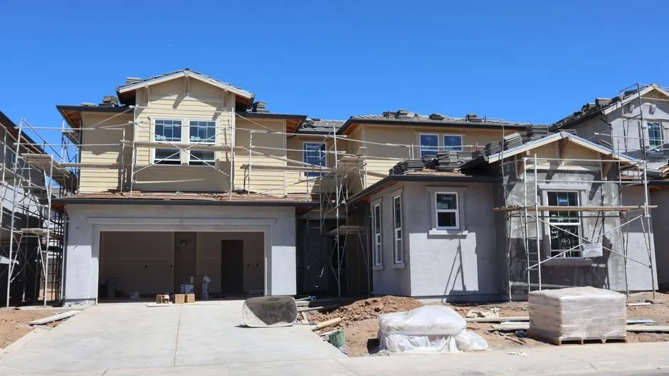 A large, modern house under construction with scaffolding against a clear blue sky.
