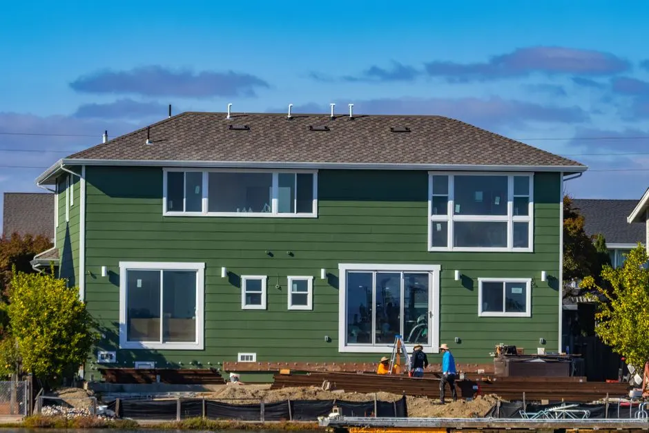 A modern green house under construction with blue skies and workers outside.