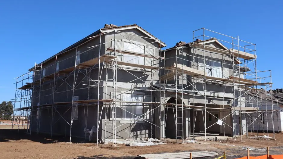 A new two-story house under construction with scaffolding on a clear day.